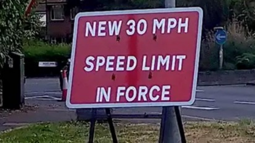 A picture with a sign that says "New 30MPH Speed limit in force"